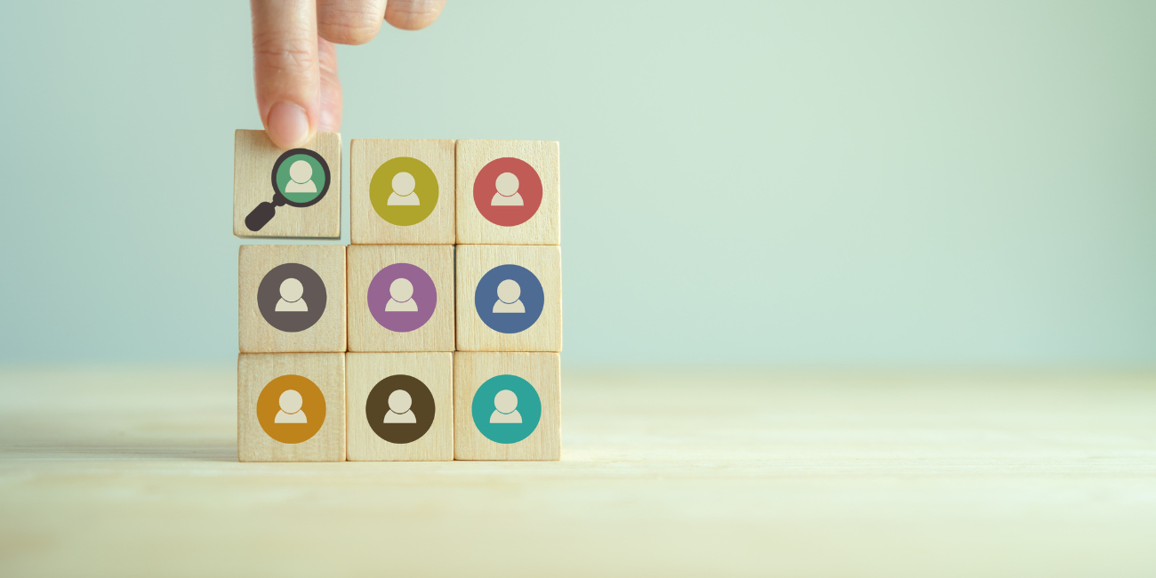 Colorful person icons on blocks stacked together, one has a magnifying glass around it